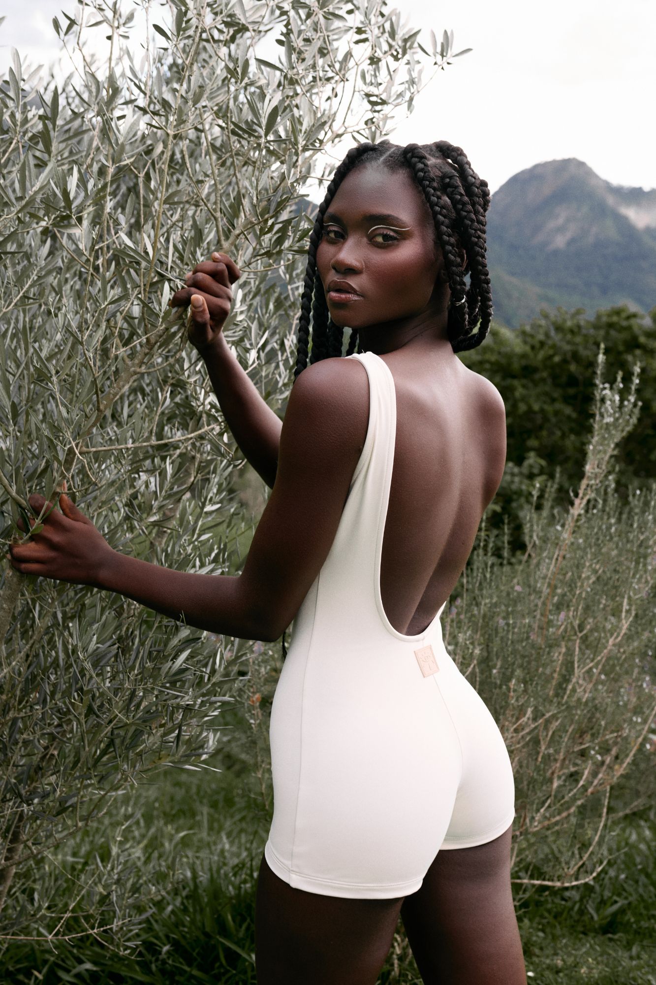Mulher negra com tranças usando body YAMONÉ branco em meio à natureza.